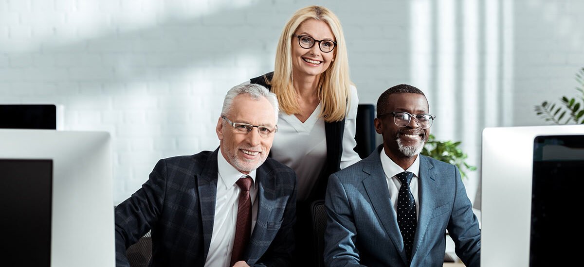 Three smiling colleagues at office computers