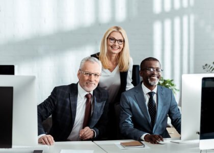 Three smiling colleagues at office computers
