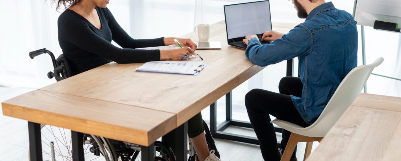 Woman in wheelchair meeting colleague at desk